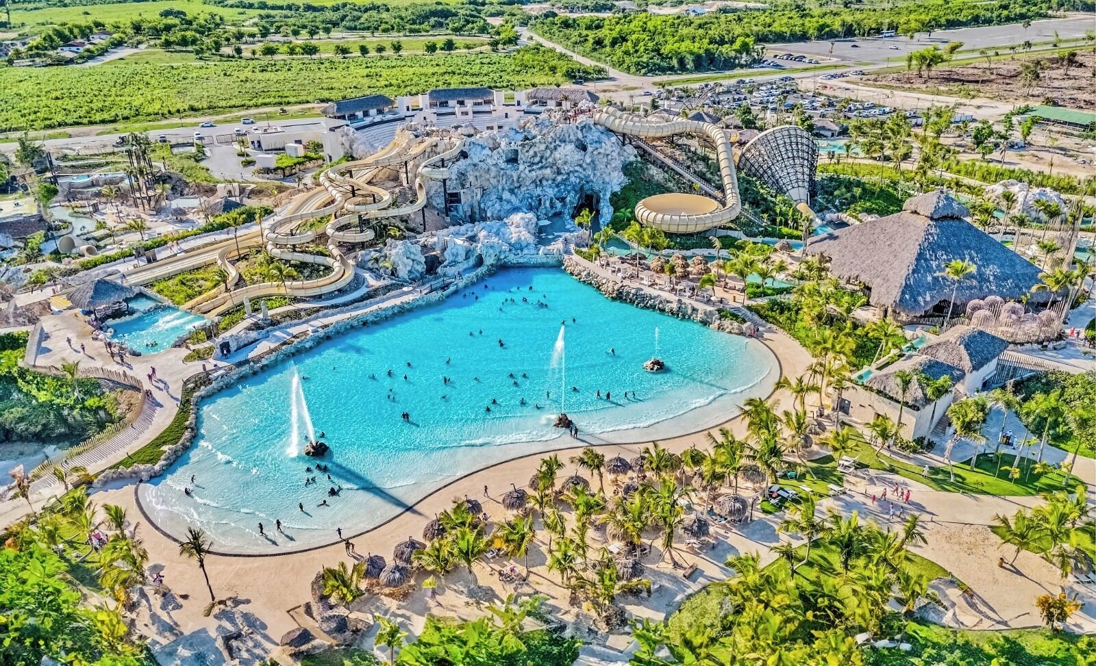 Une grande piscine extérieure dotée de plusieurs éléments aquatiques, entourée de palmiers et d’un paysage tropical.