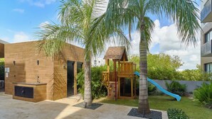 A modern outdoor area with a play structure, a wooden bench, and a small building with a slide.
