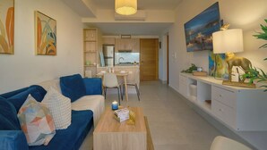 A modern living room with a blue sofa, a coffee table, and a dining area with a white table and chairs.