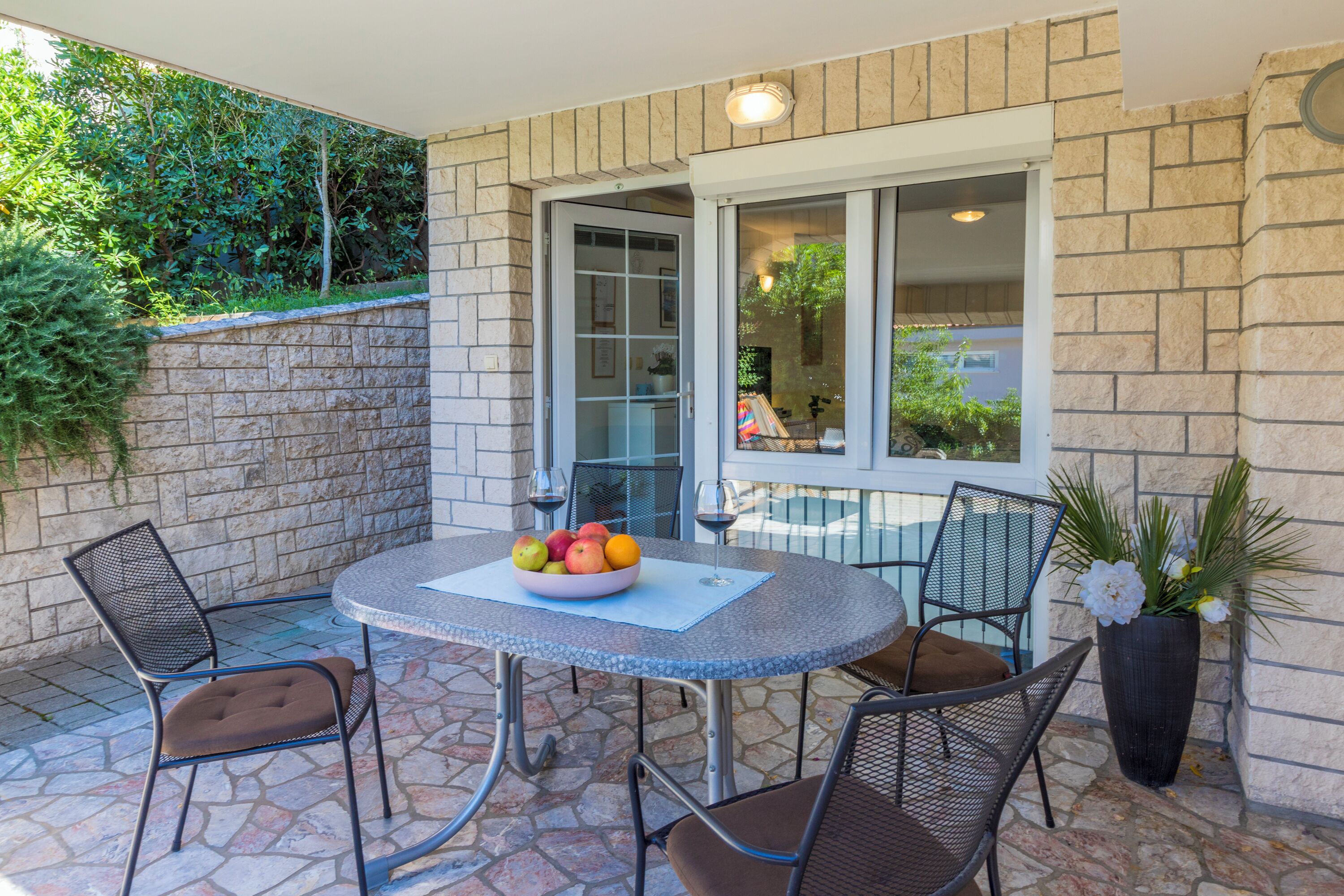 Une terrasse extérieure avec une table ronde, quatre chaises, un panier de fruits et une plante en pot.