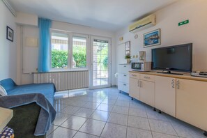 A room with a bed, a TV, a kitchenette, and a window with a view of greenery. - Studio for 2 with terrace, barbecue, parking lot (Crikvenica)