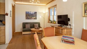 A cozy living room with a sofa, a dining table, a TV, and a painting on the wall. - NaturLogis-Allgäu in the organic claywood house Healthy living - living without pollutants (Nesselwang)