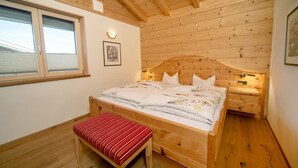 A wooden-paneled bedroom with a bed, bench, bedside table, and wall-mounted light. - NaturLogis-Allgäu in the organic claywood house Healthy living - living without pollutants (Nesselwang)