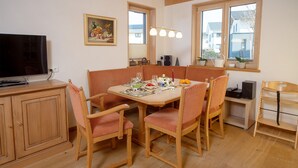 A dining area with a wooden table and chairs, a television on a cabinet, and a painting on the wall. - NaturLogis-Allgäu in the organic claywood house Healthy living - living without pollutants (Nesselwang)