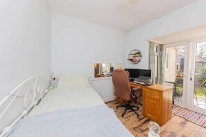 Un dormitorio con una cama, un escritorio con computadora, una silla, una ventana y una puerta.