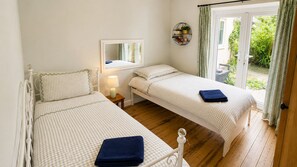 A bedroom with two single beds, a bedside table with a lamp, a mirror, and a view of a garden through a sliding door. - Bright & spacious 3-bedroom bungalow with garden (Brundall)