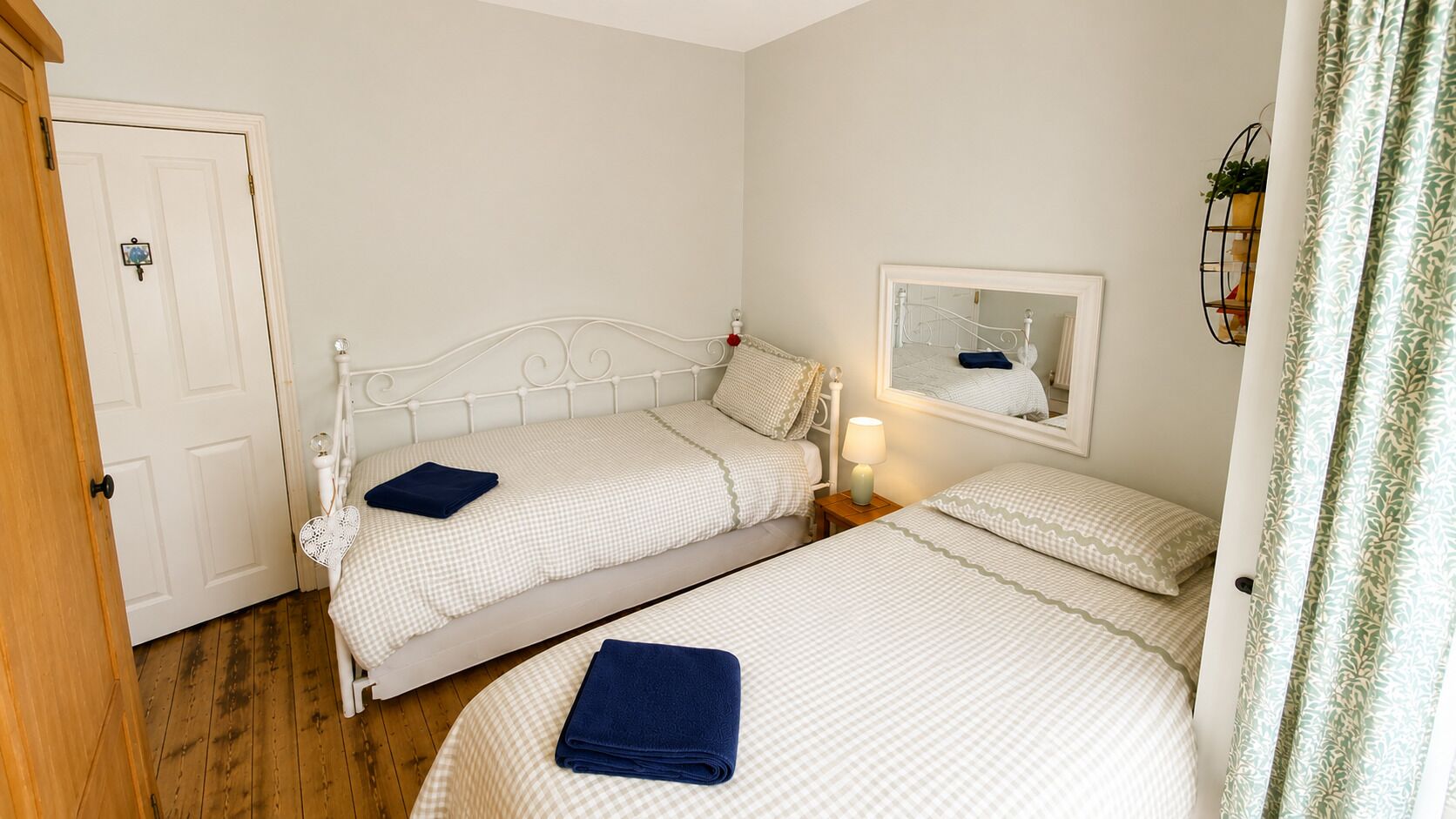 Een slaapkamer met twee eenpersoonsbedden, een nachtkastje met een lamp, een spiegel en een deur.