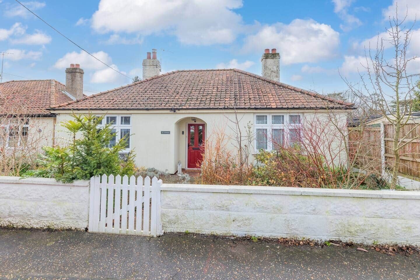 Eenlaags huis met een rode deur, een witte hek en een heldere lucht.