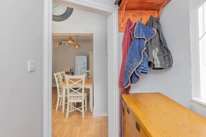 Un pasillo estrecho con un banco de madera, un comedor con mesa y sillas, y un perchero con abrigos.
