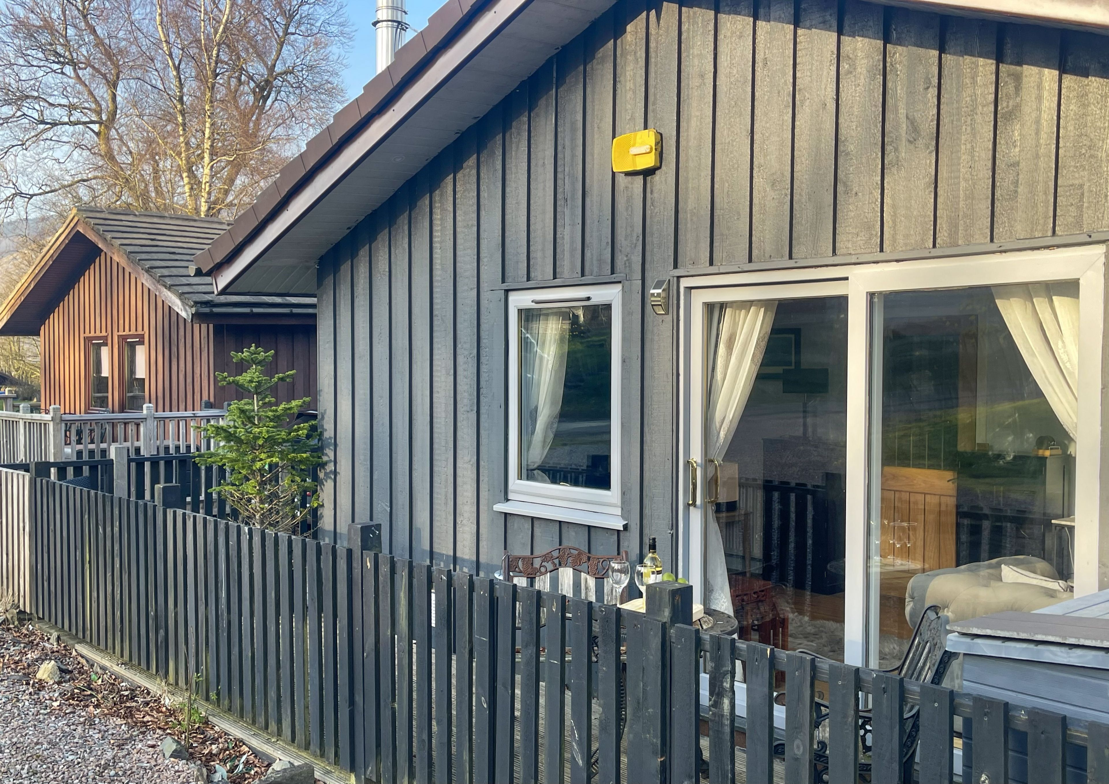 Eine Holzhütte mit umzäuntem Garten, einem Fenster und einer Tür mit Vorhängen.