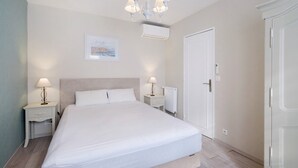 A bedroom with a bed, two bedside tables with lamps, a ceiling light fixture, a door, and an air conditioning unit. - Juan-les-Pins Vitoria Grand 2P – Quiet, Parking, Central Location (Antibes)