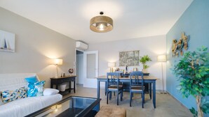 A modern living room with a sofa, coffee table, and dining area with chairs and a table. - Juan-les-Pins Vitoria Grand 2P – Quiet, Parking, Central Location (Antibes)