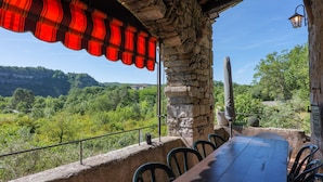 A stone table with chairs, a red awning, and a view of a forested valley.