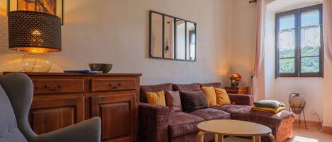 A living room with a sofa, a chair, a table, a lamp, a mirror, and a window with curtains.