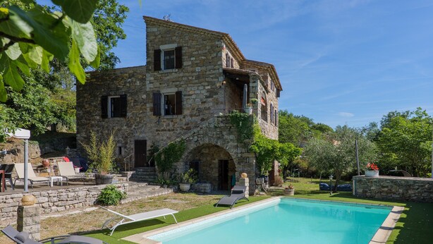 A stone building with a swimming pool, outdoor seating, and greenery.