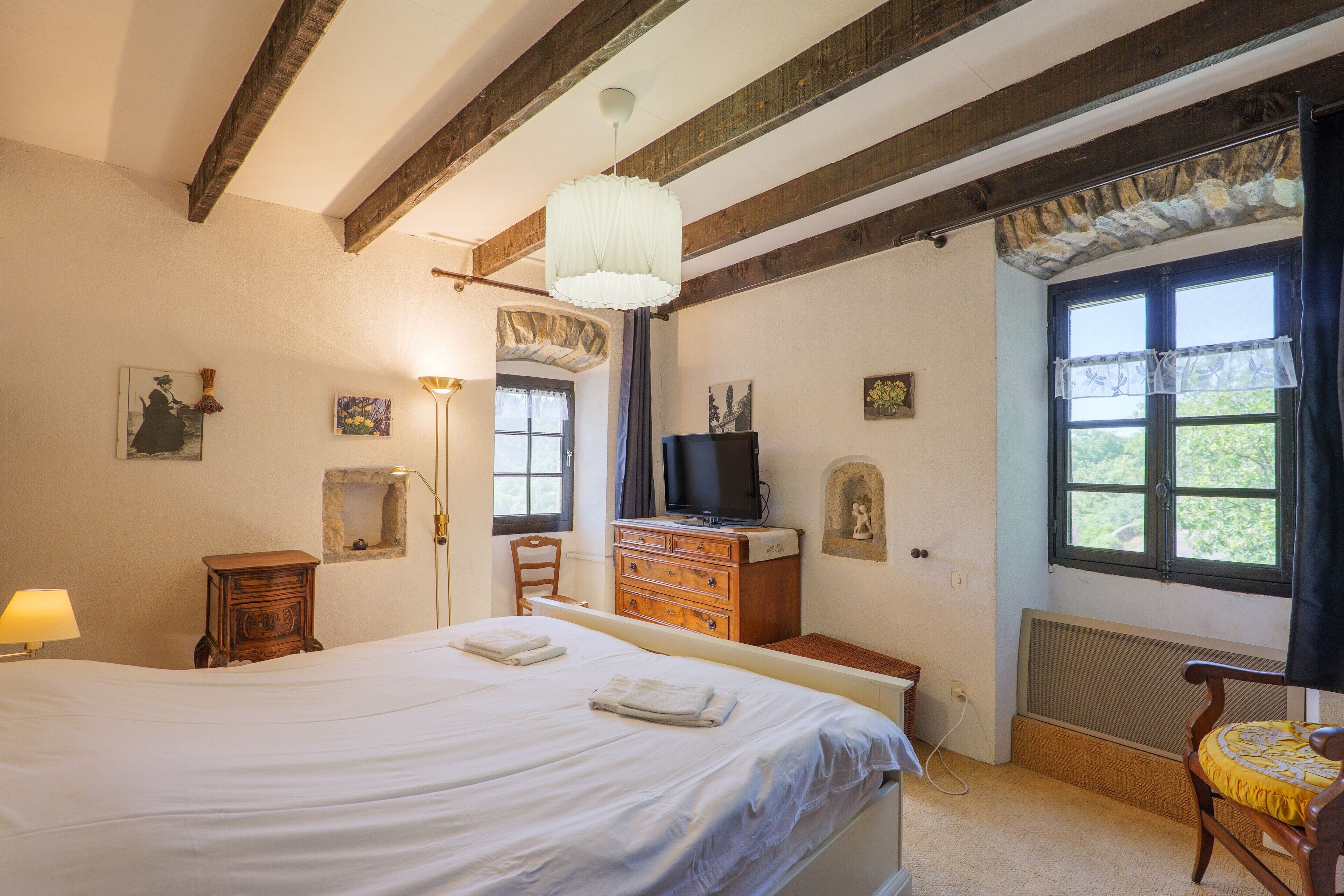 Une chambre à coucher avec un grand lit, une commode en bois, une télévision et une fenêtre donnant sur un beau paysage.