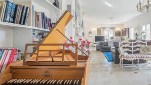A living room with a grand piano, bookshelves, a sofa, and a chandelier. - Charming bed and breakfast in Giono country. (Manosque)