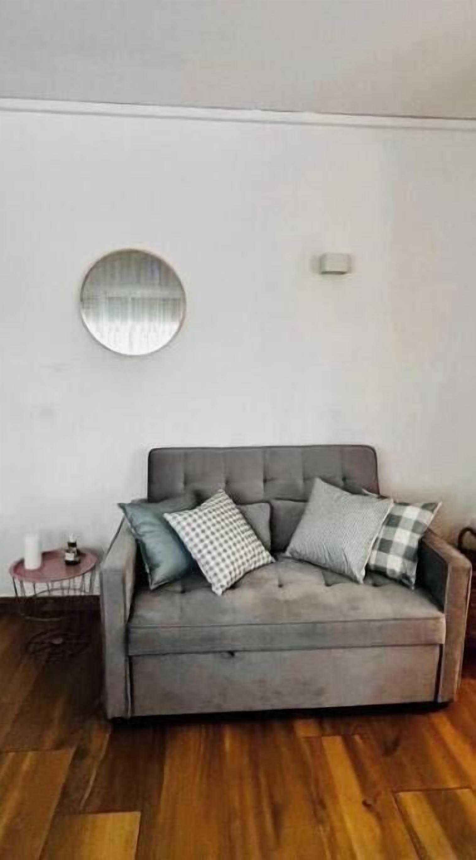 Un canapé gris agrémenté de plusieurs coussins, un miroir rond accroché au mur et une petite table sur laquelle est posée une bougie.
