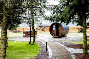 Eine rustikale Holzhütte mit einer tonnenförmigen Struktur, umgeben von Bäumen und einem Holzzaun.