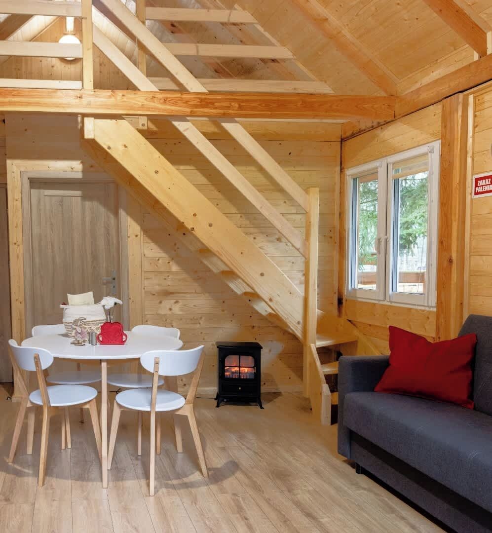 Een houten interieur met een eettafel, stoelen, een bank, een open haard en een trap.