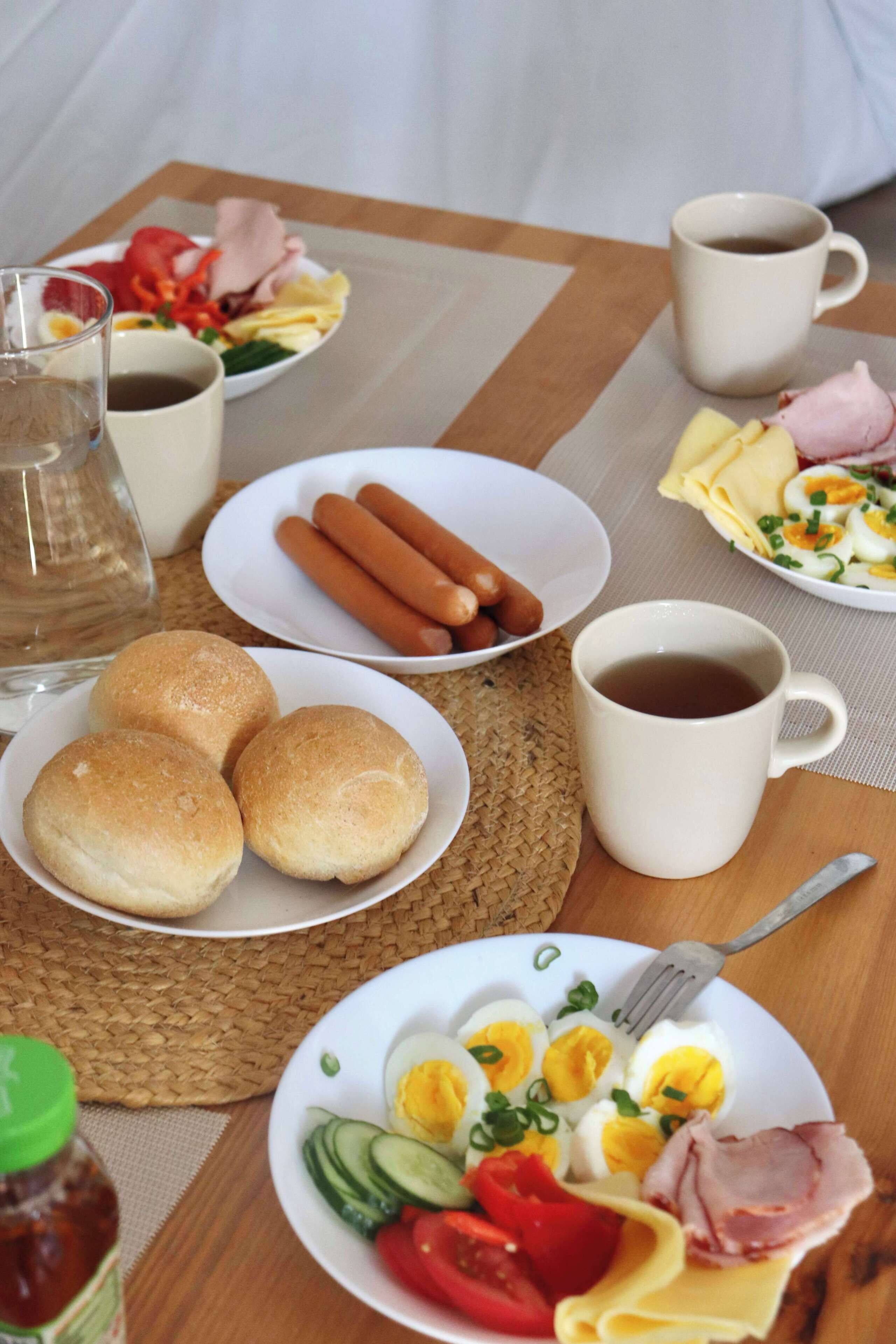 A breakfast table with plates of food, a coffee mug, and a bottle of sauce.