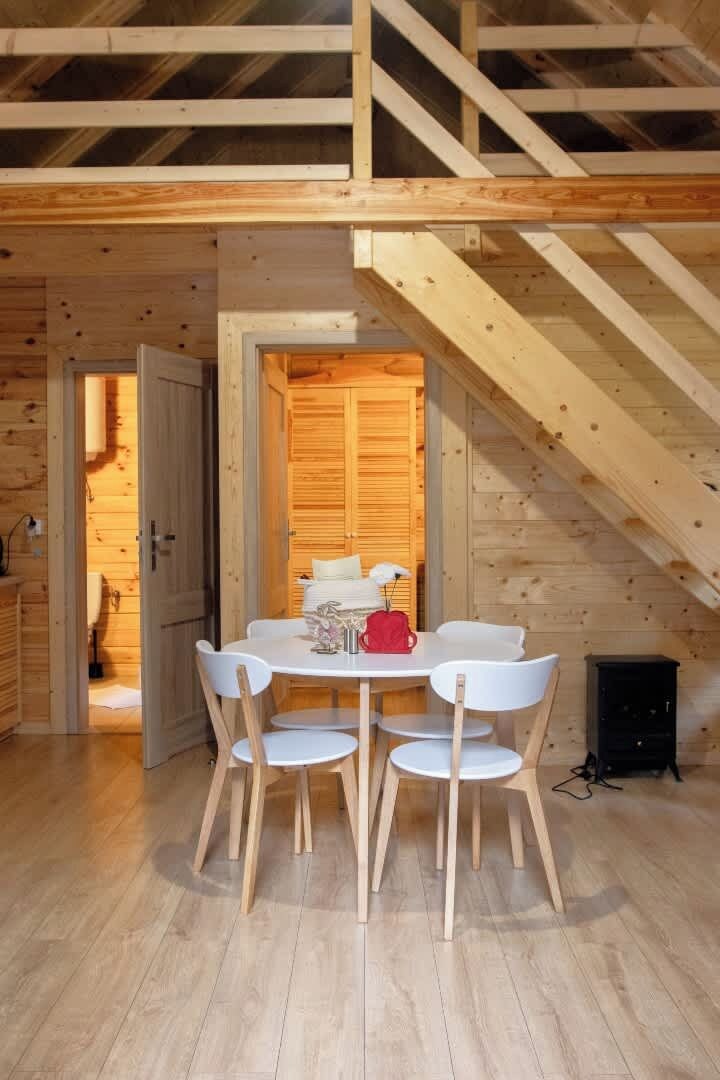 Een houten interieur met een eettafel en stoelen, een trap en een deur die naar een andere kamer leidt.