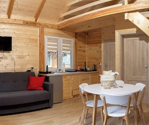 Interior acogedor de una cabaña con sofá, mesa de comedor y zona de cocina.