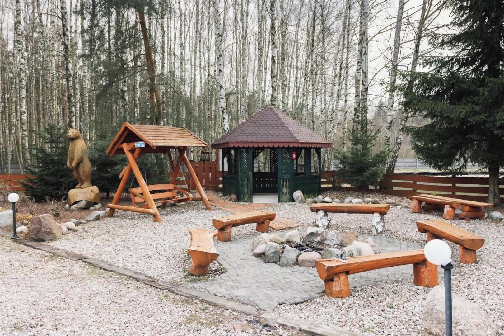 A wooden swing set, a gazebo, and benches in a forested area.