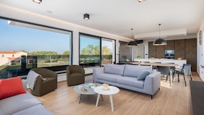 Een moderne woonkamer met een bank, fauteuils, een salontafel en een eethoek, met een keuken op de achtergrond.