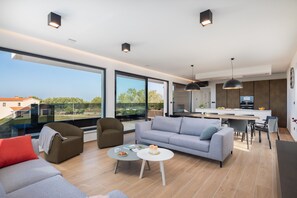 Ein modernes Wohnzimmer mit einer Couch, Sesseln, einem Couchtisch und einem Essbereich mit einer Küche im Hintergrund.