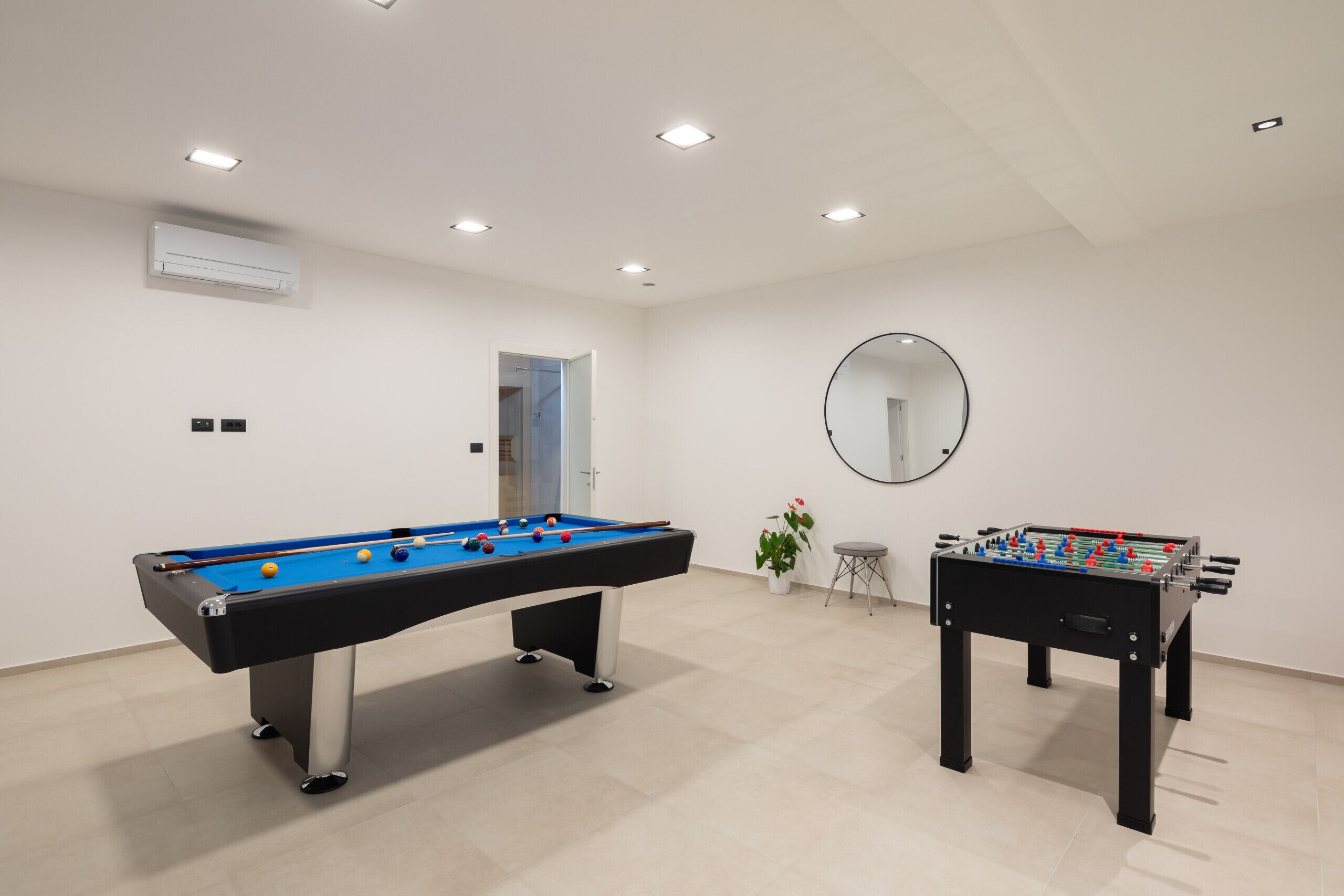 Una habitación con mesa de billar, mesa de fútbol y espejo, además de una puerta que da a otra estancia.