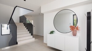 Een moderne trap met een minimalistisch ontwerp, een ronde spiegel op een witte console, en een potplant.