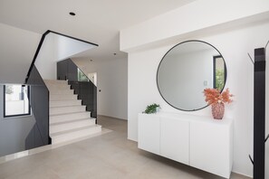 Eine moderne Treppe mit minimalistischem Design, ein runder Spiegel auf einer weißen Konsole und ein Blumentopf.