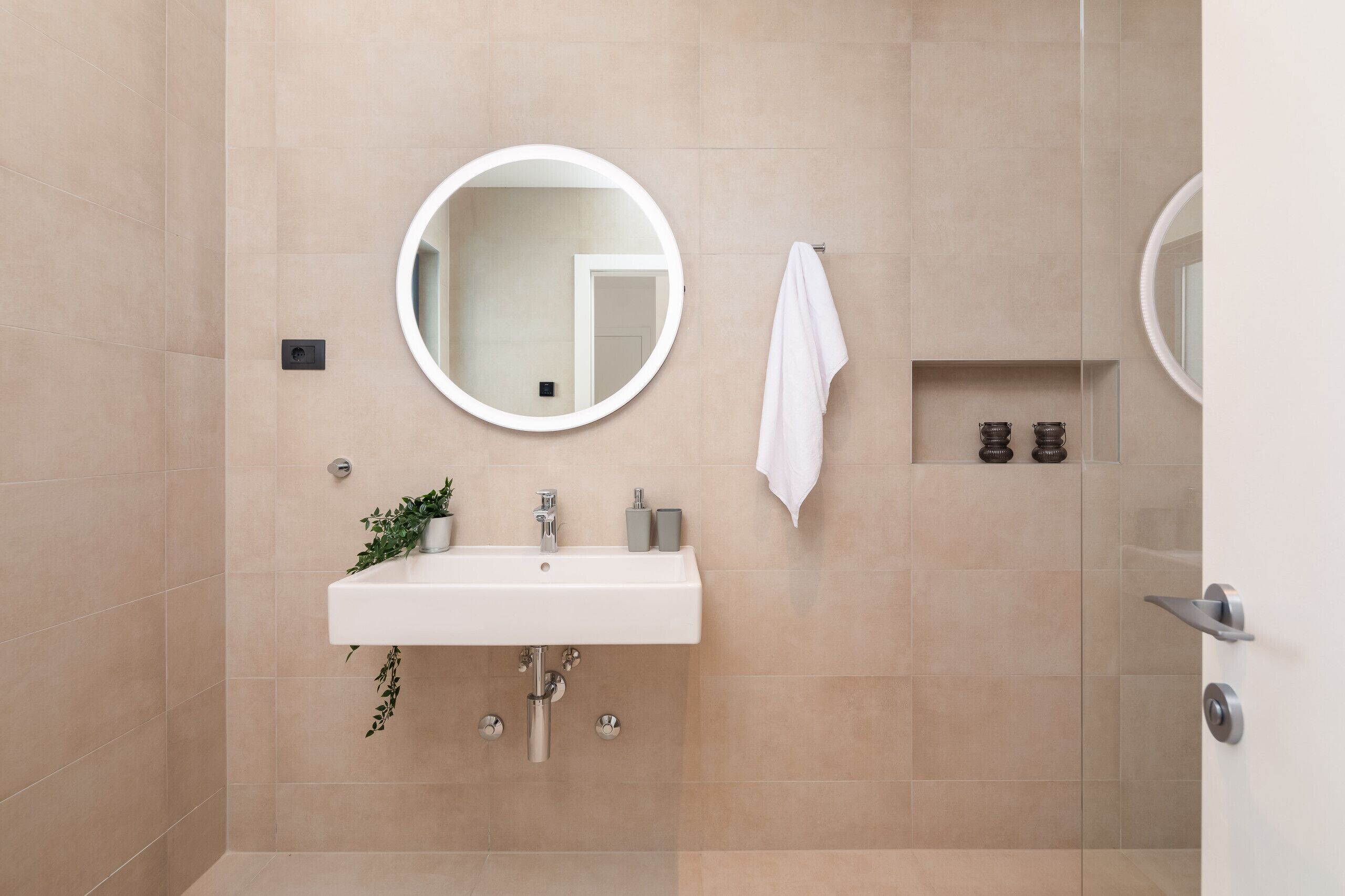 Ein modernes Badezimmer mit einem weißen Waschbecken, zwei runden Spiegeln, einem Handtuchhalter und einer kleinen Ablage mit Pflegeprodukten.