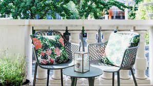Un balcon avec deux chaises et une table, entouré d’une balustrade blanche et de verdure.