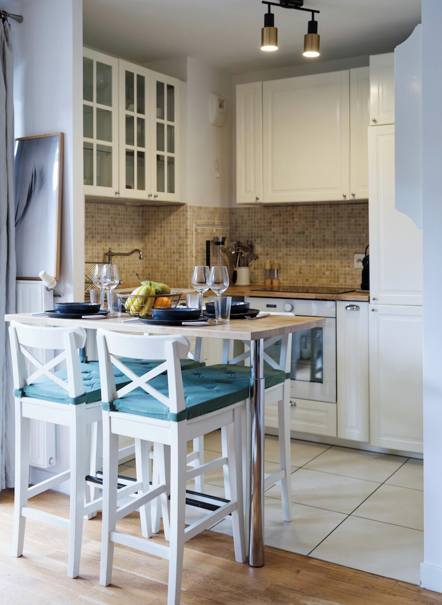 A modern kitchen with white cabinets, a dining table with chairs, and a hanging light fixture.