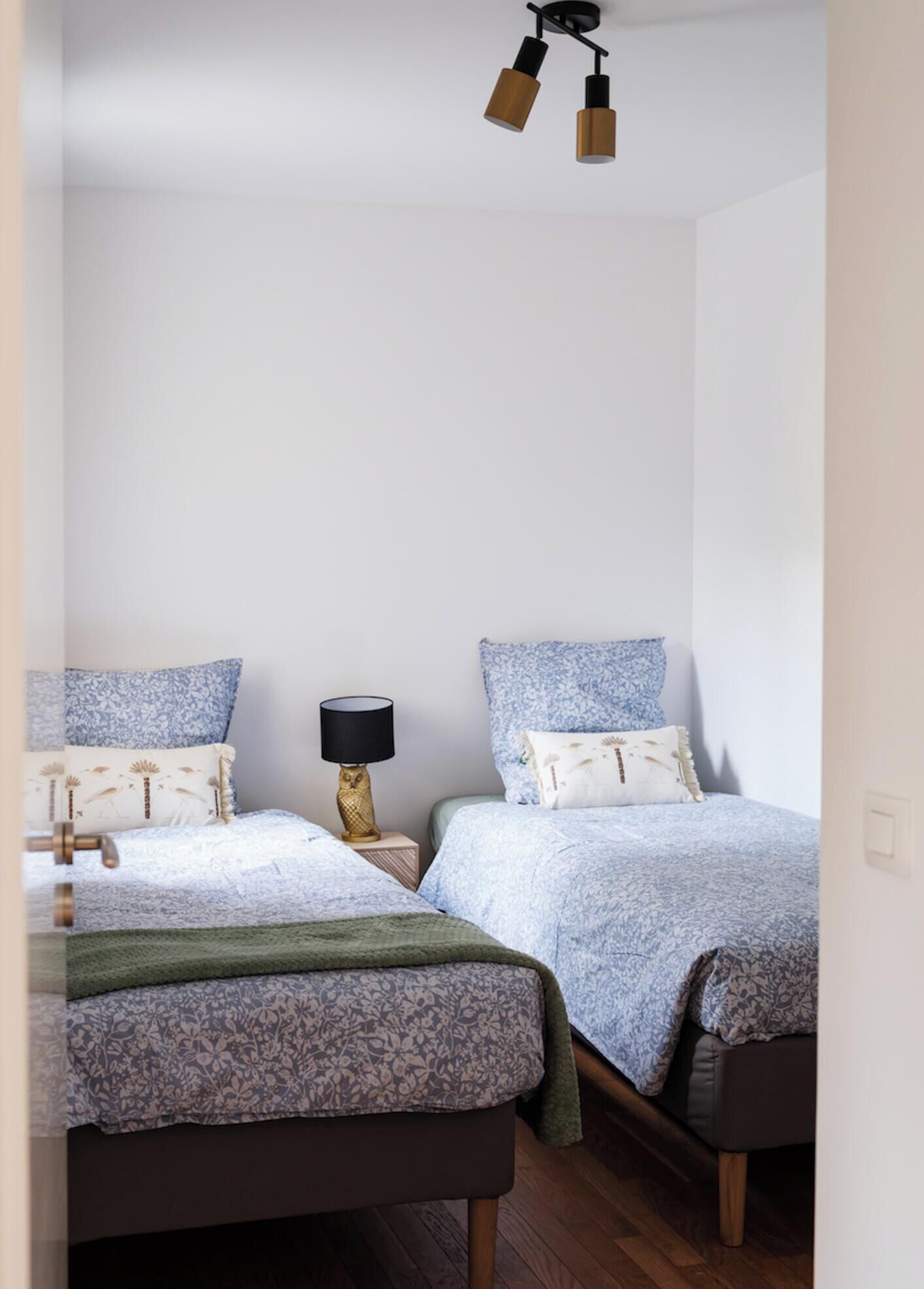 A bedroom with two beds, a nightstand with a lamp, and a ceiling light fixture.