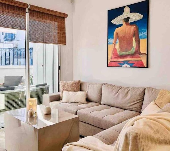 Un salon moderne avec un canapé, une table basse en verre et un tableau représentant une personne sur une plage.