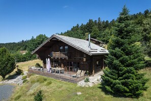 Una cabaña de troncos con balcón, mobiliario exterior y vista a un área boscosa.