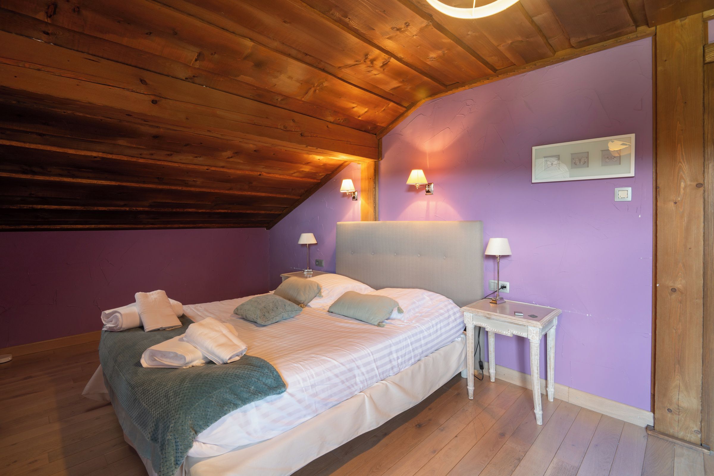 Un dormitorio con techo de madera, una cama con ropa blanca, dos lámparas de noche y una mesita de noche.