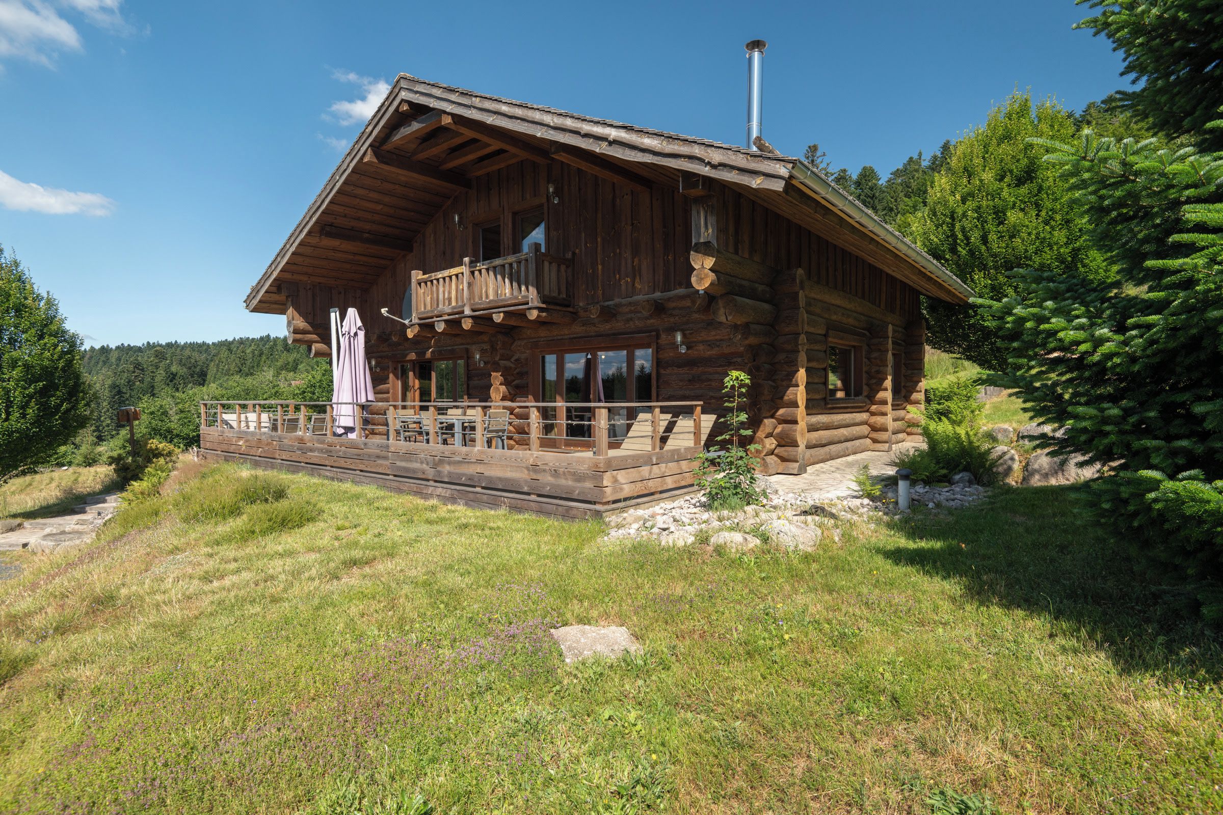 A log cabin with a balcony, wooden deck, and a chimney.
