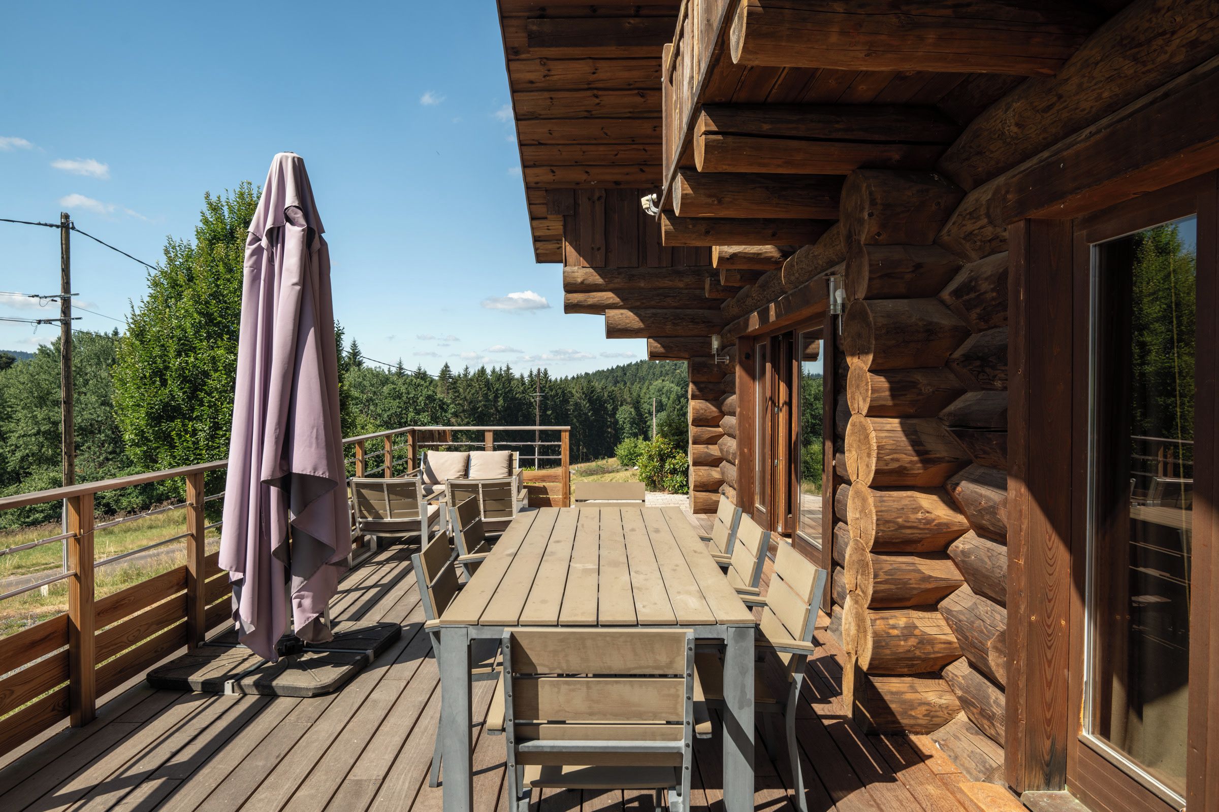 Une terrasse en bois avec des meubles d’extérieur, un espace salon abrité et une vue sur la forêt environnante.