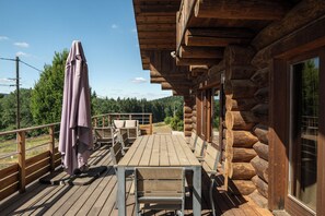 Een houten terras met buitenmeubilair, een overdekte zithoek en uitzicht op het omliggende bos.