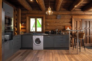 A modern kitchen with a built-in washing machine, wooden cabinetry, and a bar area with stools. - Chalet Serenity - Sleeps 9 - Hot Tub (Liézey)
