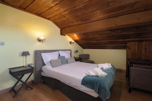 A bedroom with a wooden ceiling, a bed with white bedding, two bedside lamps, and a chair. - Chalet Serenity - Sleeps 9 - Hot Tub (Liézey)