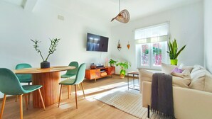 A modern living room with a wooden dining table, green chairs, a sofa, and a TV mounted on the wall. - 2 bedrooms. Roman Amphitheater. Near the beach (Tarragona)