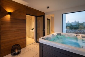 Ein modernes Badezimmer mit Holzwand, einer Duschkabine aus Glas, einer Badewanne und Blick ins Freie.