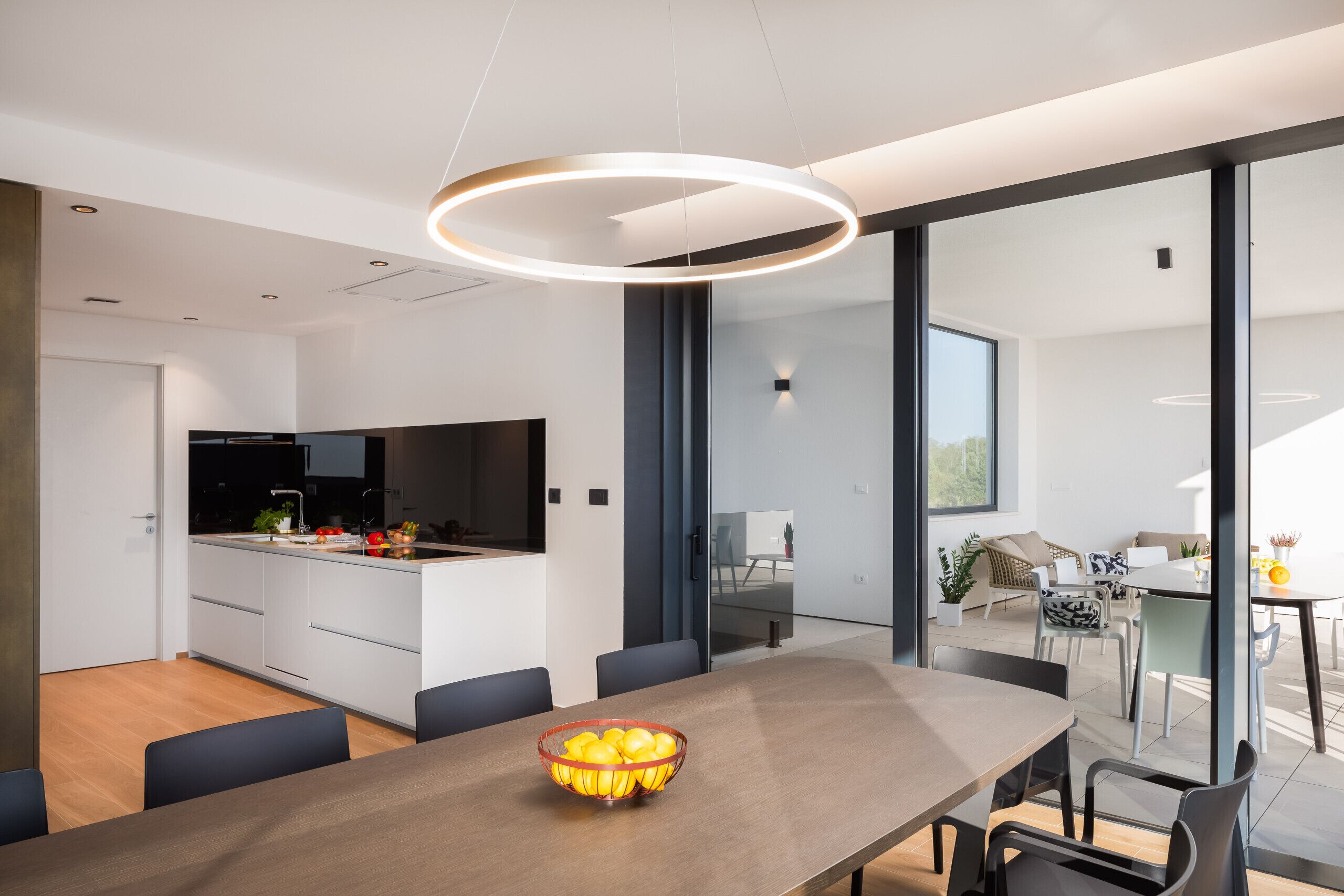 Una cocina moderna con una isla grande, un comedor con una mesa larga y vistas a través de amplios ventanales.