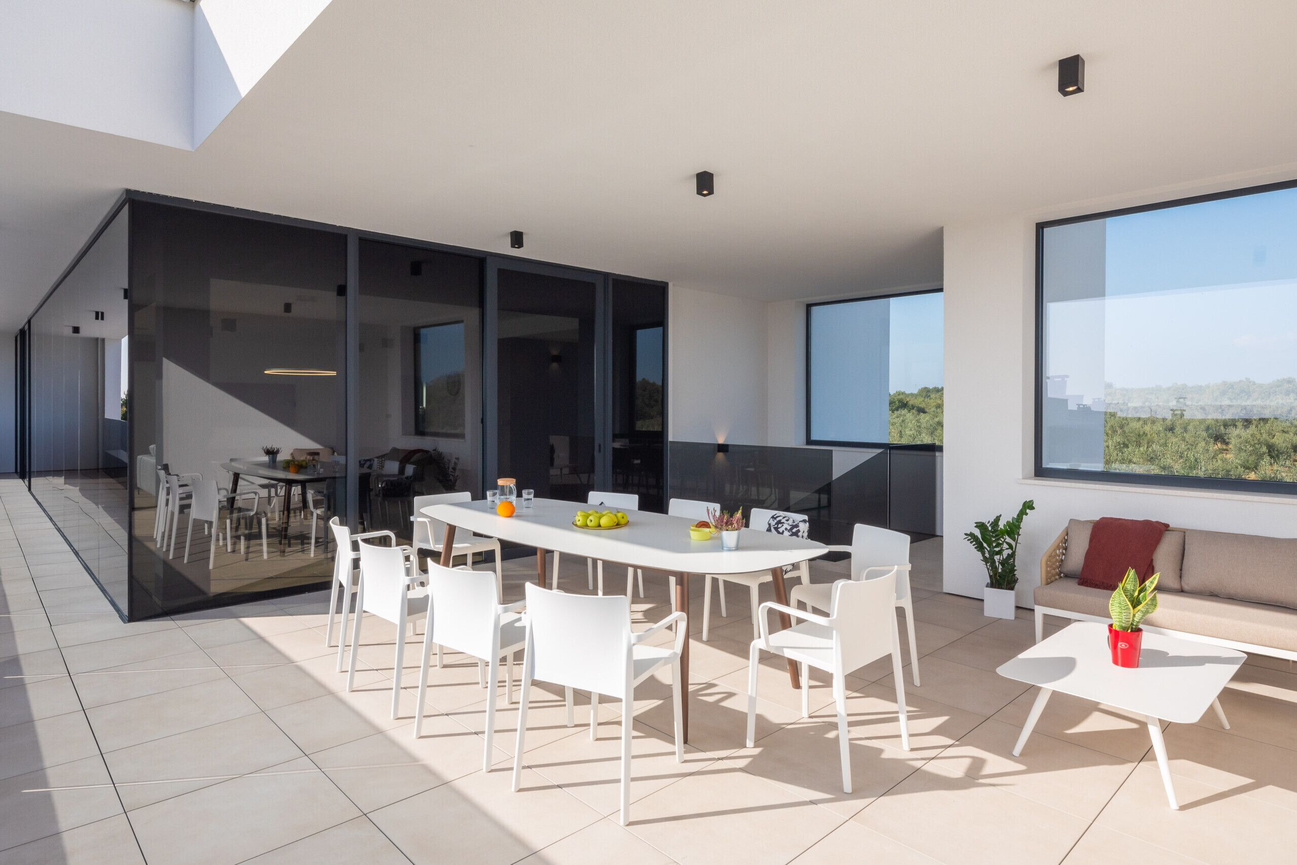 Un espacio exterior moderno para comer con mesa y sillas blancas, un sofá y una planta en maceta.