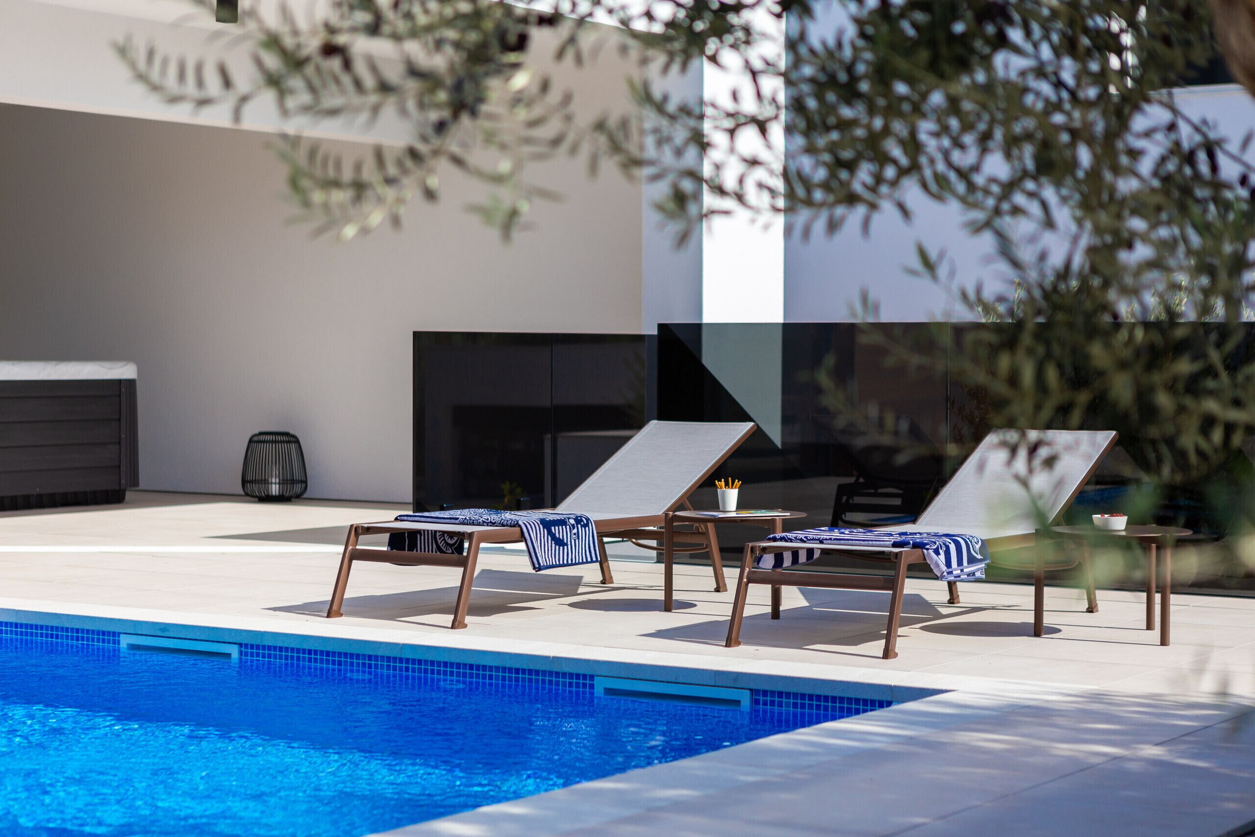 Un espace piscine extérieur moderne, doté de chaises longues et d’un foyer.